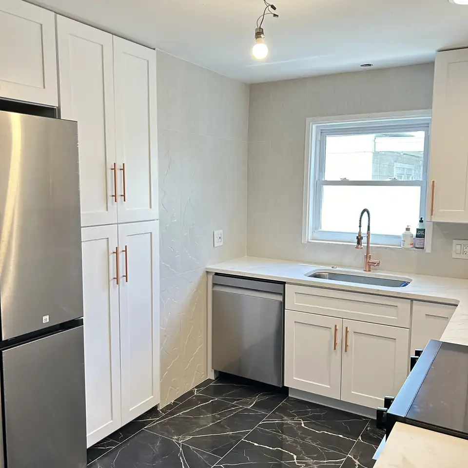 Kitchen remodeling Largo FL: white shaker cabinets with copper pulls, white quartz counters, black marble-look floor tile and stainless appliances