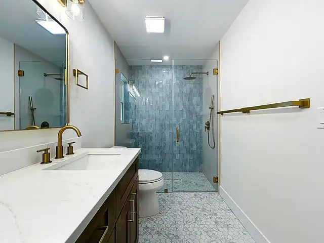 Belleair bathroom with walnut vanity, white quartz top, brass faucet and a blue tile walk-in shower with hex mosaic floor
