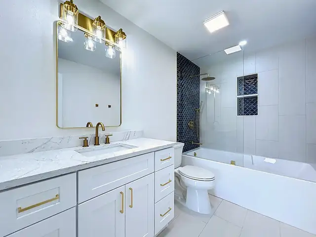 Belleair bathroom with white shaker vanity, brass hardware, arched mirror and a navy tile niche above the tub