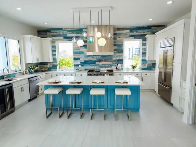 White shaker kitchen with a custom aqua island, gold-base bar stools and a blue glass tile wall behind the range hood