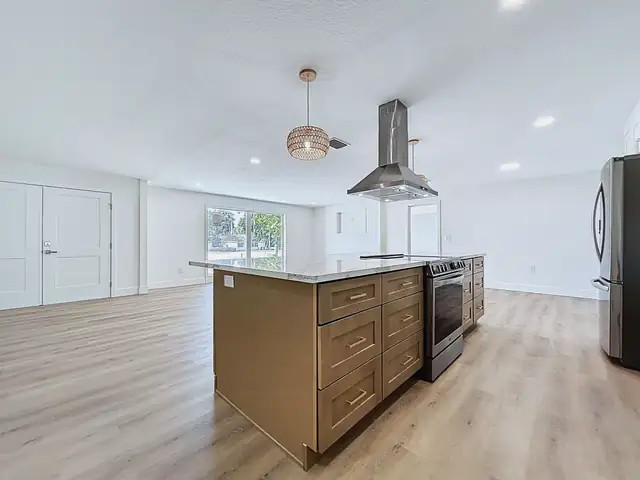 Open kitchen with a natural wood shaker island, island range under a stainless hood, brass pendant and quartz counters