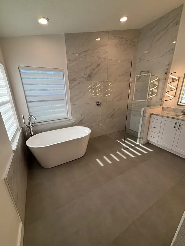 Wet room with a freestanding tub, large-format stone-look tile and a frameless glass enclosure