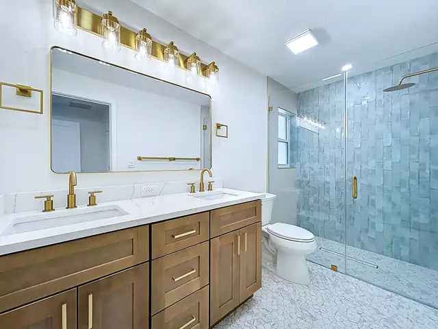 Belleair Beach primary bathroom with wood double vanity, brass light bars and a seafoam tile walk-in shower