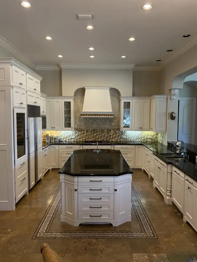 Refinished white raised-panel kitchen by Bayshore Remodels with a black granite island, a white hood and a tile floor medallion